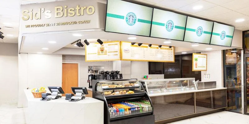 Mostrador de Sid's Bistro con un letrero de We Proudly Serve Starbucks Coffee, pizarras de menú y una vitrina de repostería