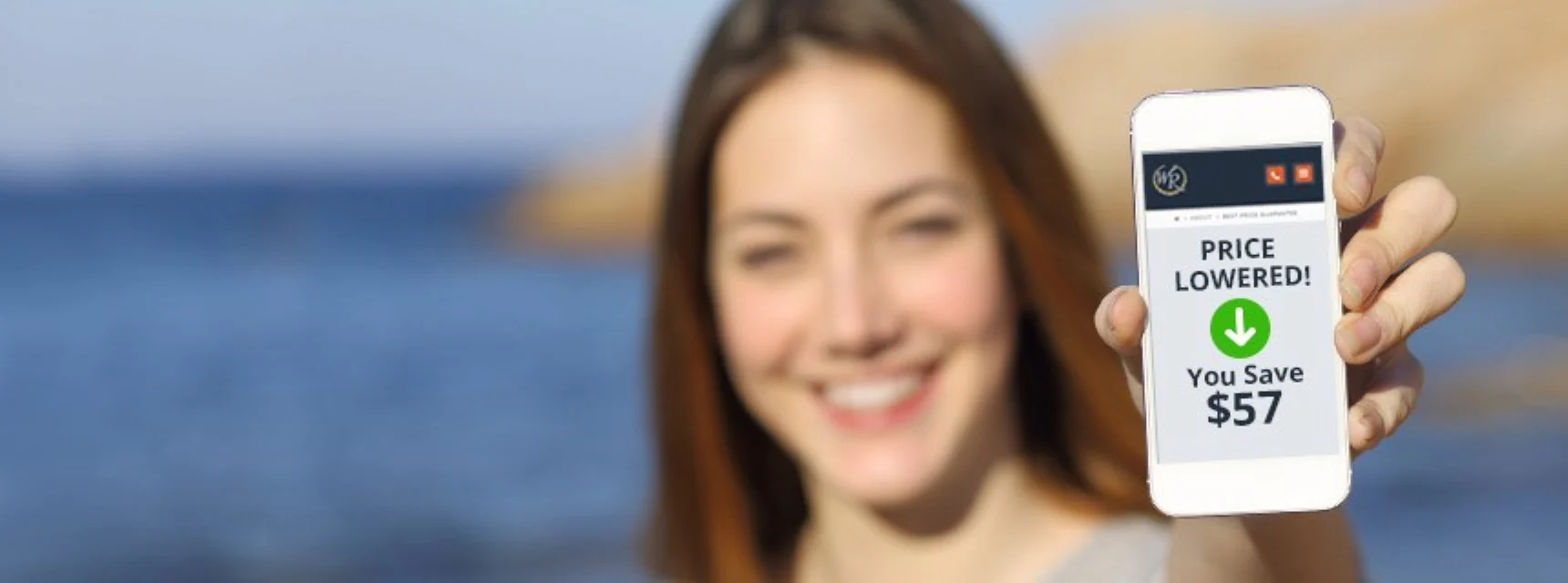 Smiling woman on the beach holding a phone showing a lowered Westgate vacation price