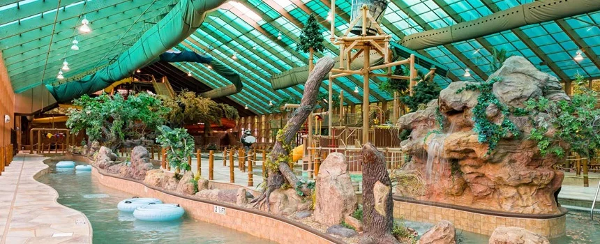 Lazy river winding past rockwork and trees under the glass roof of Wild Bear Falls indoor water park